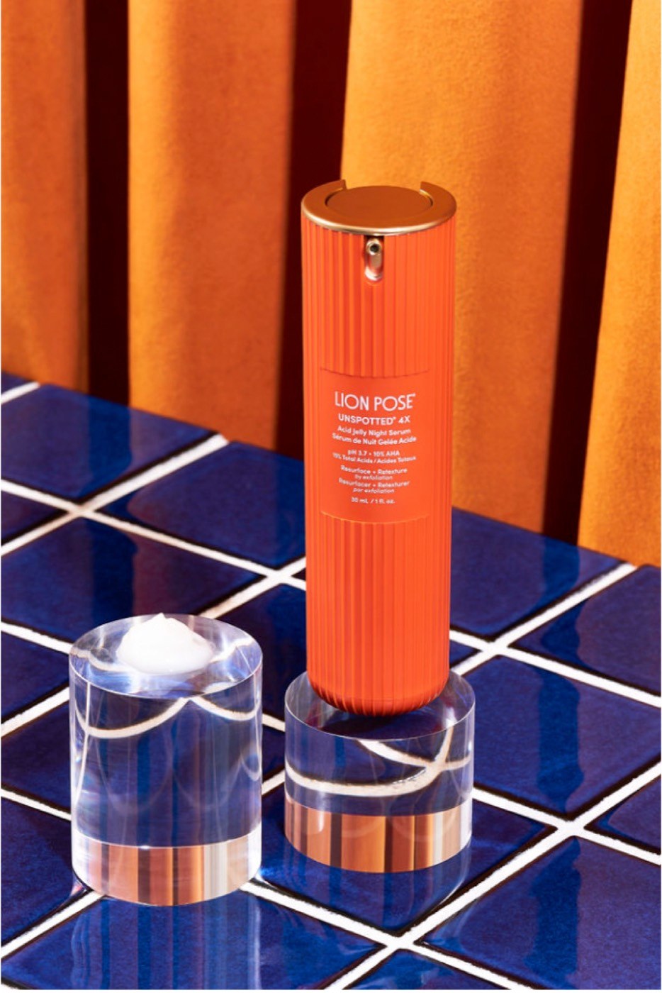 Lion Pose serum on acrylic against an orange curtain